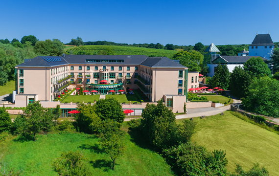 Das Hotel liegt im Sonnenlicht, an einer Straße mit grünen Bäumen.