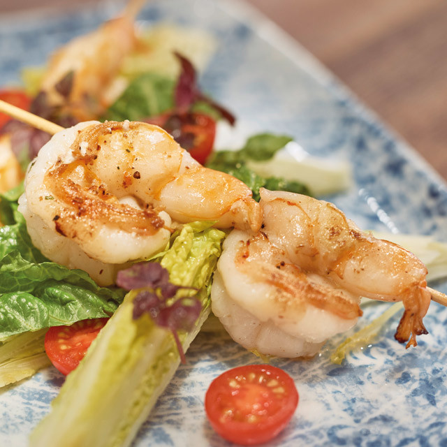 Eine Collage zeigt links das Restaurant The Club München und rechts einen eingedeckten Tisch. Auf dem Tisch steht ein heißer Stein mit Rumpsteak, eine Schale Pommes frites, sowie Caprese-Salat.